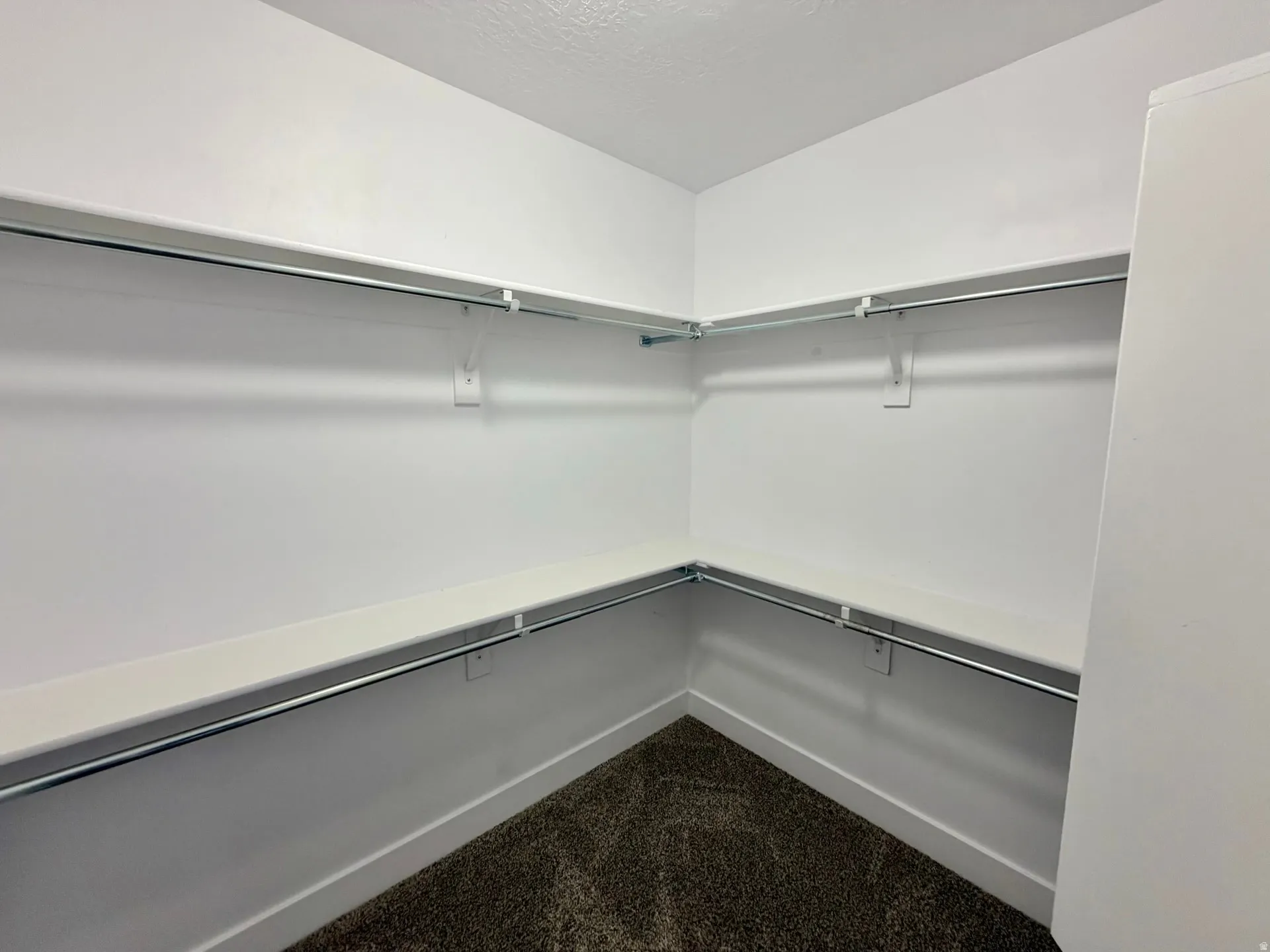 Walk-in closet featuring white painted walls, white shelving, chrome hanging rods, and dark carpeting