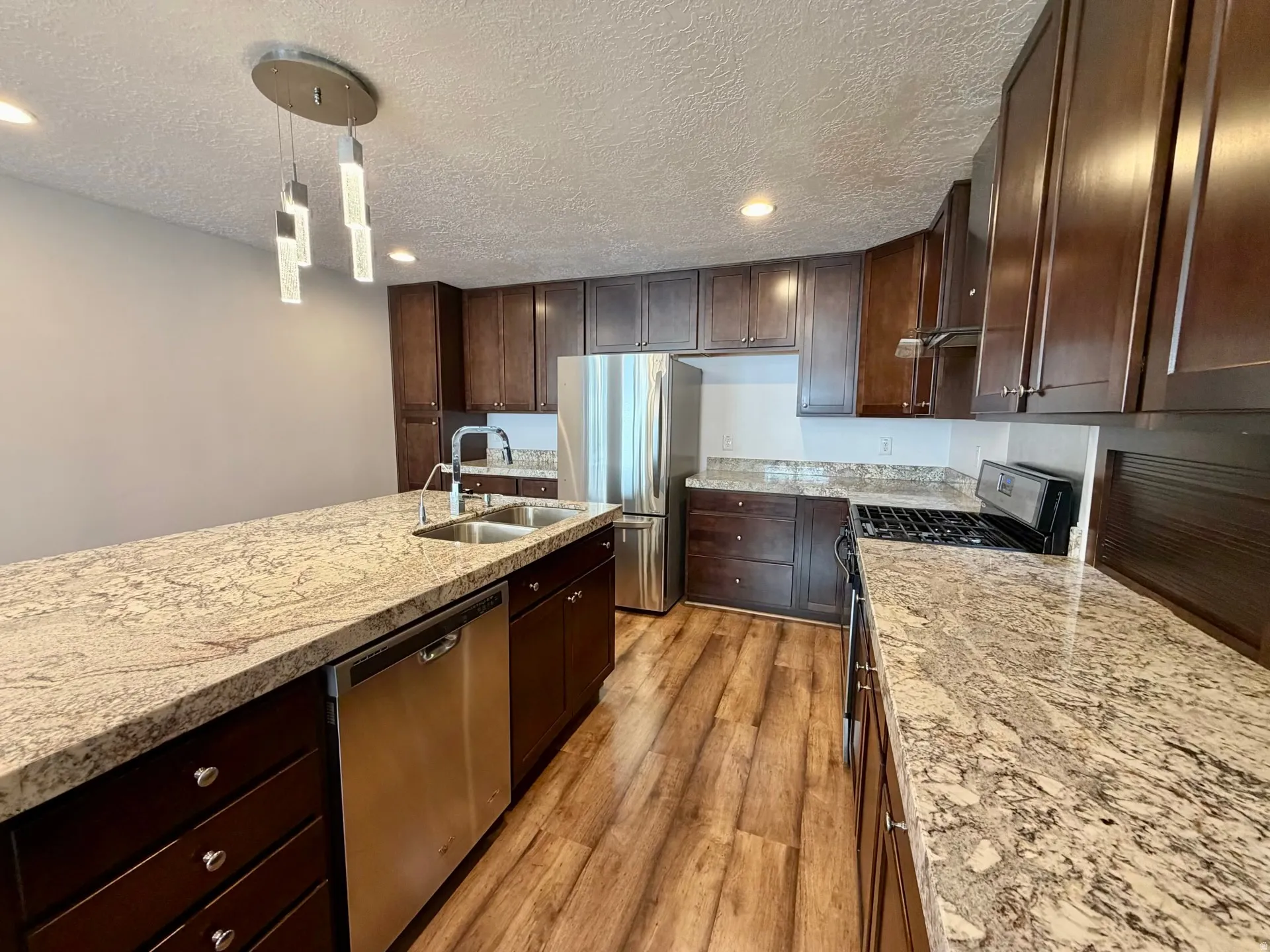 Kitchen featuring a central island with granite-finish countertops, dark wood cabinetry, a stainless steel double sink, and a stainless steel dishwasher