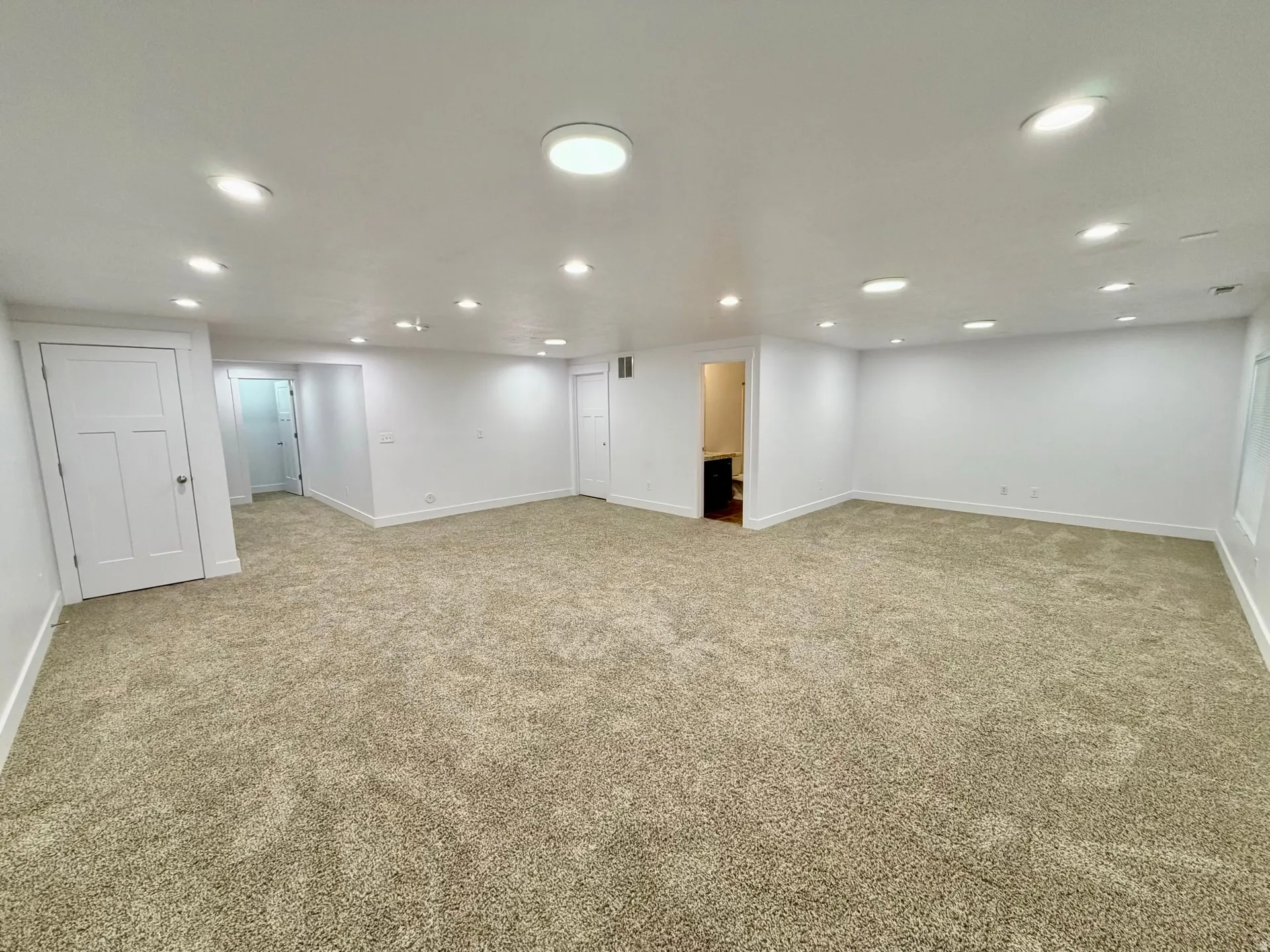 Spacious room featuring new carpeting, recessed lighting, white walls, white baseboards, and multiple white paneled doors