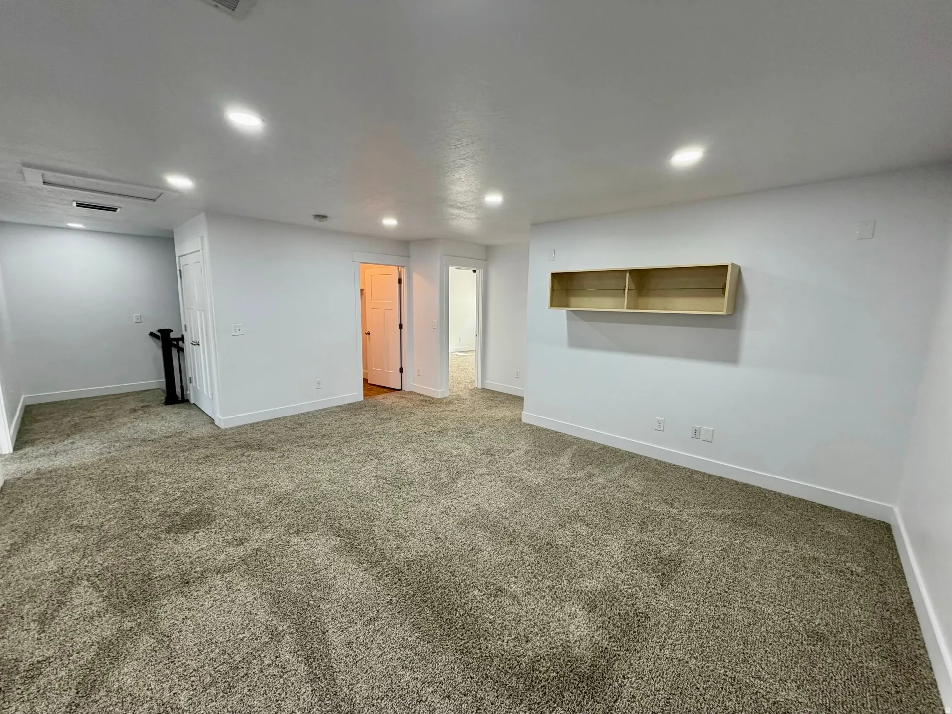 Spacious finished basement featuring neutral carpeting throughout, recessed ceiling lighting, and built-in wall shelving