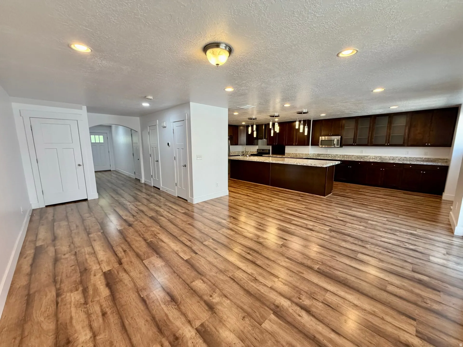Spacious interior featuring wood-finish flooring, recessed lighting, and a kitchen with dark wood cabinetry