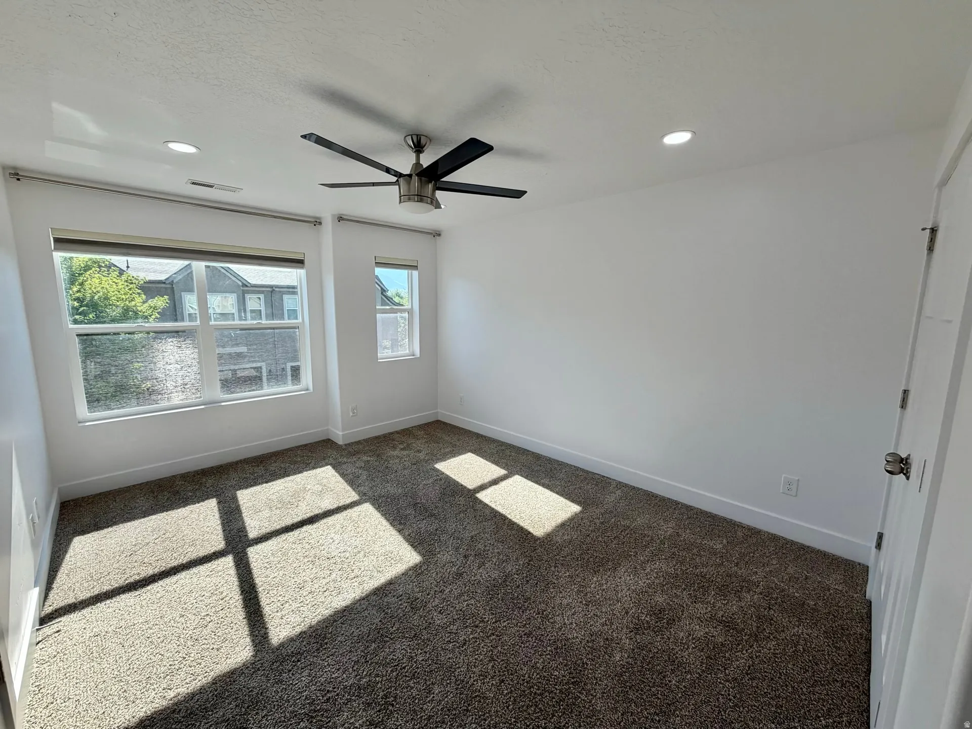 Carpeted room featuring a ceiling fan, recessed lighting, and two windows with blinds