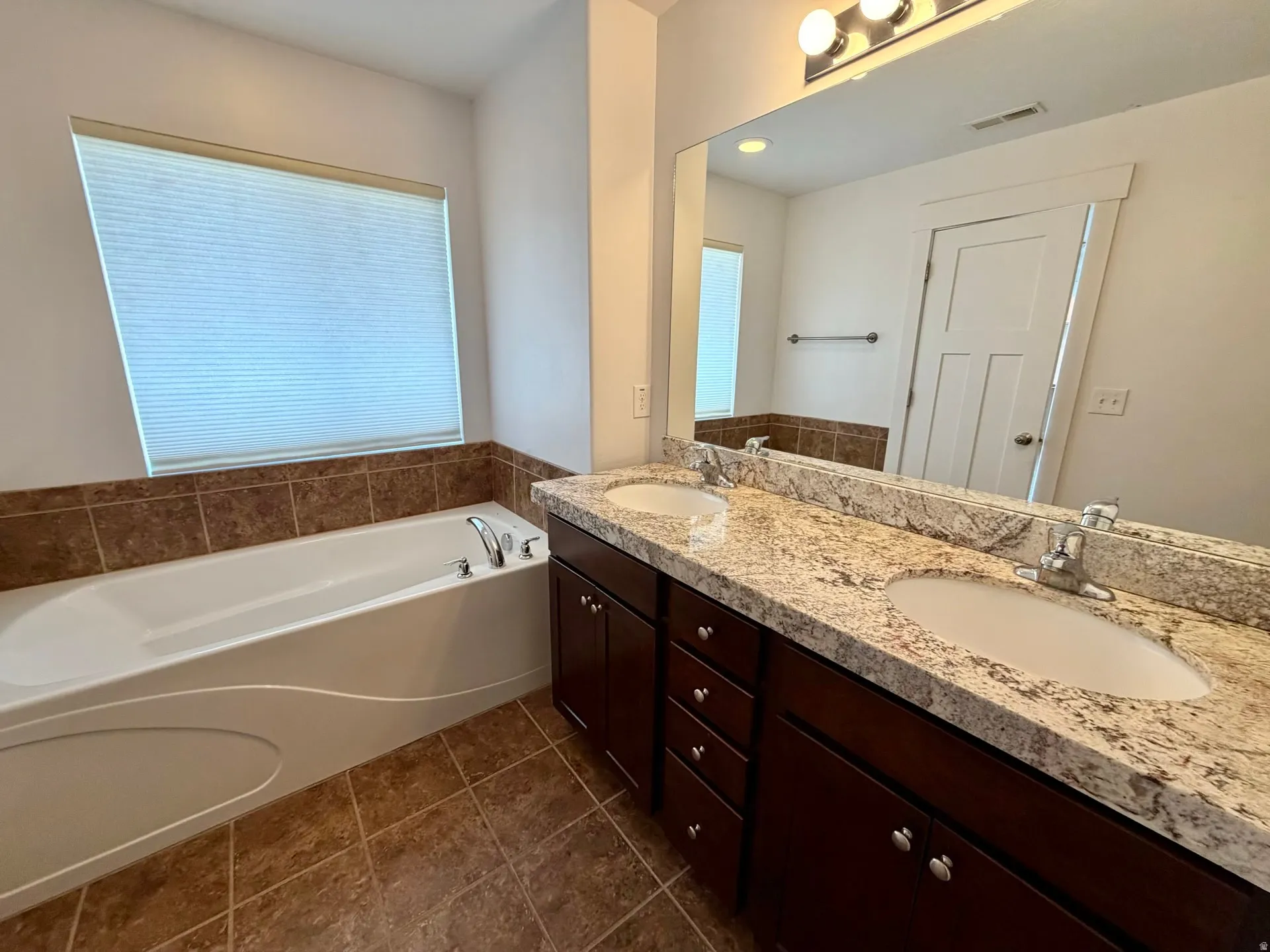 Double vanity with granite countertop and integrated sinks, complemented by a large wall-mounted mirror and sconce lighting