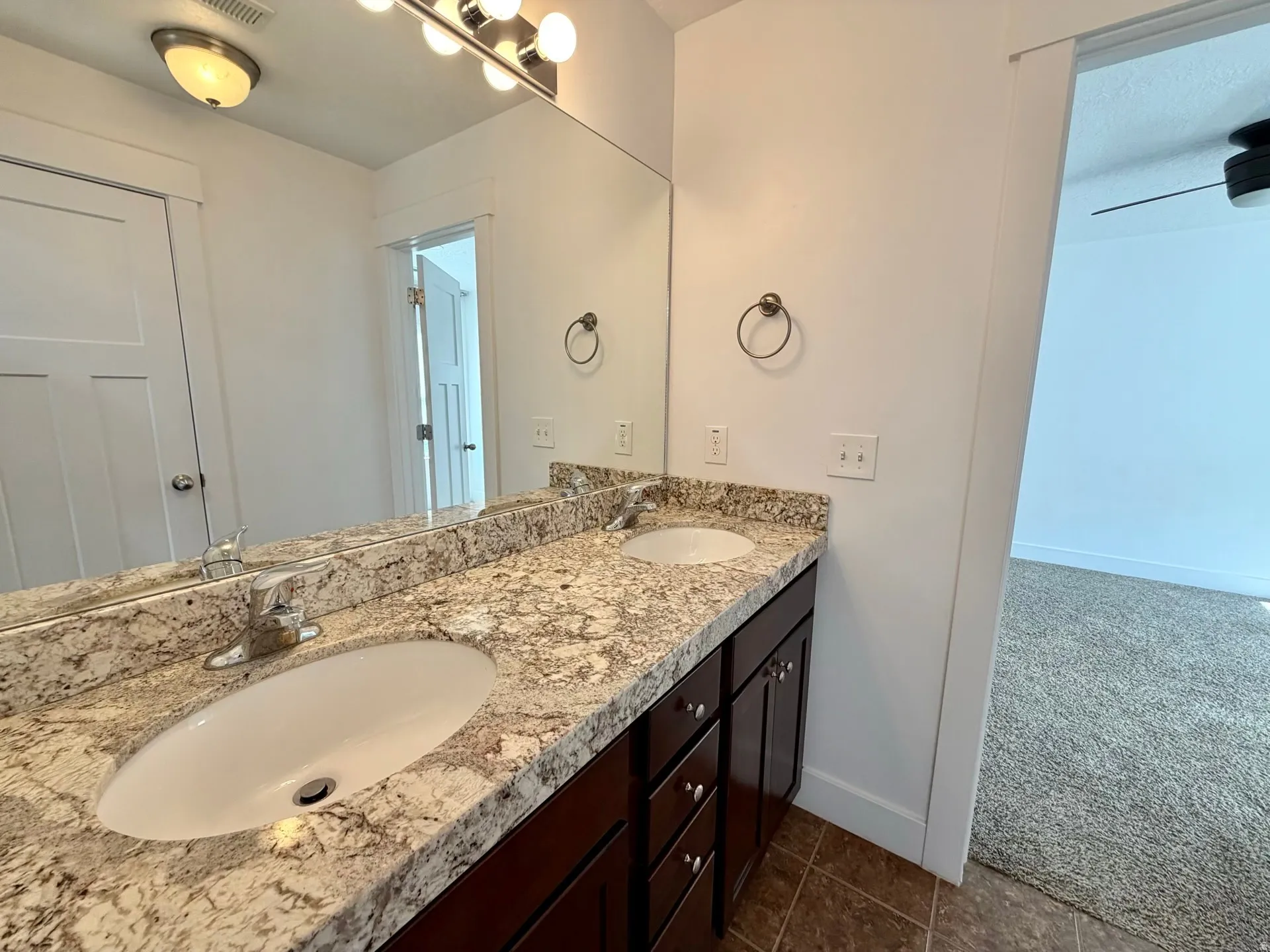Double vanity featuring a light-toned stone countertop, dual undermount sinks, and dark wood-finish cabinetry