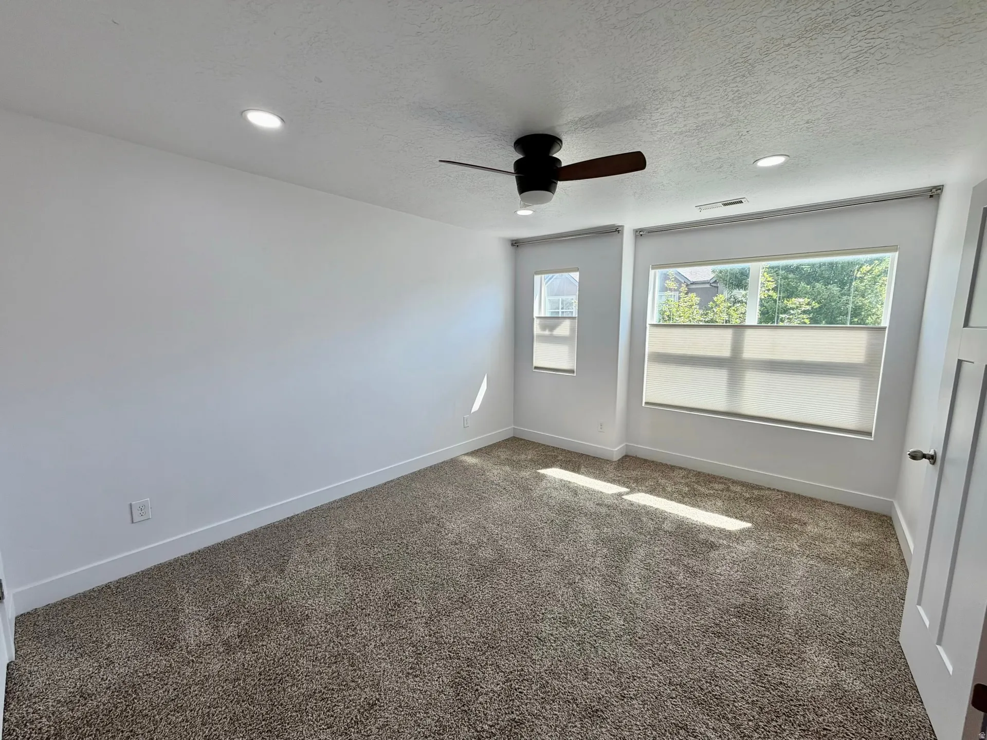 Carpeted interior space featuring recessed lighting, a ceiling fan with integrated light, and multiple windows with privacy shades