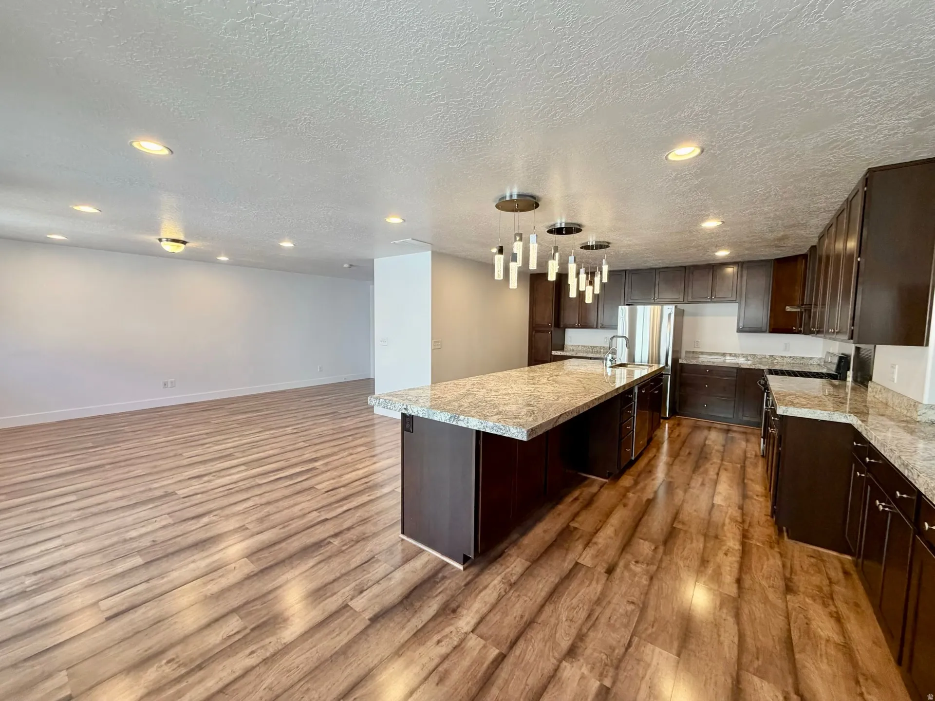 Modern kitchen featuring a large central island with a granite-style countertop, dark wood-finish cabinetry, and stainless steel appliances