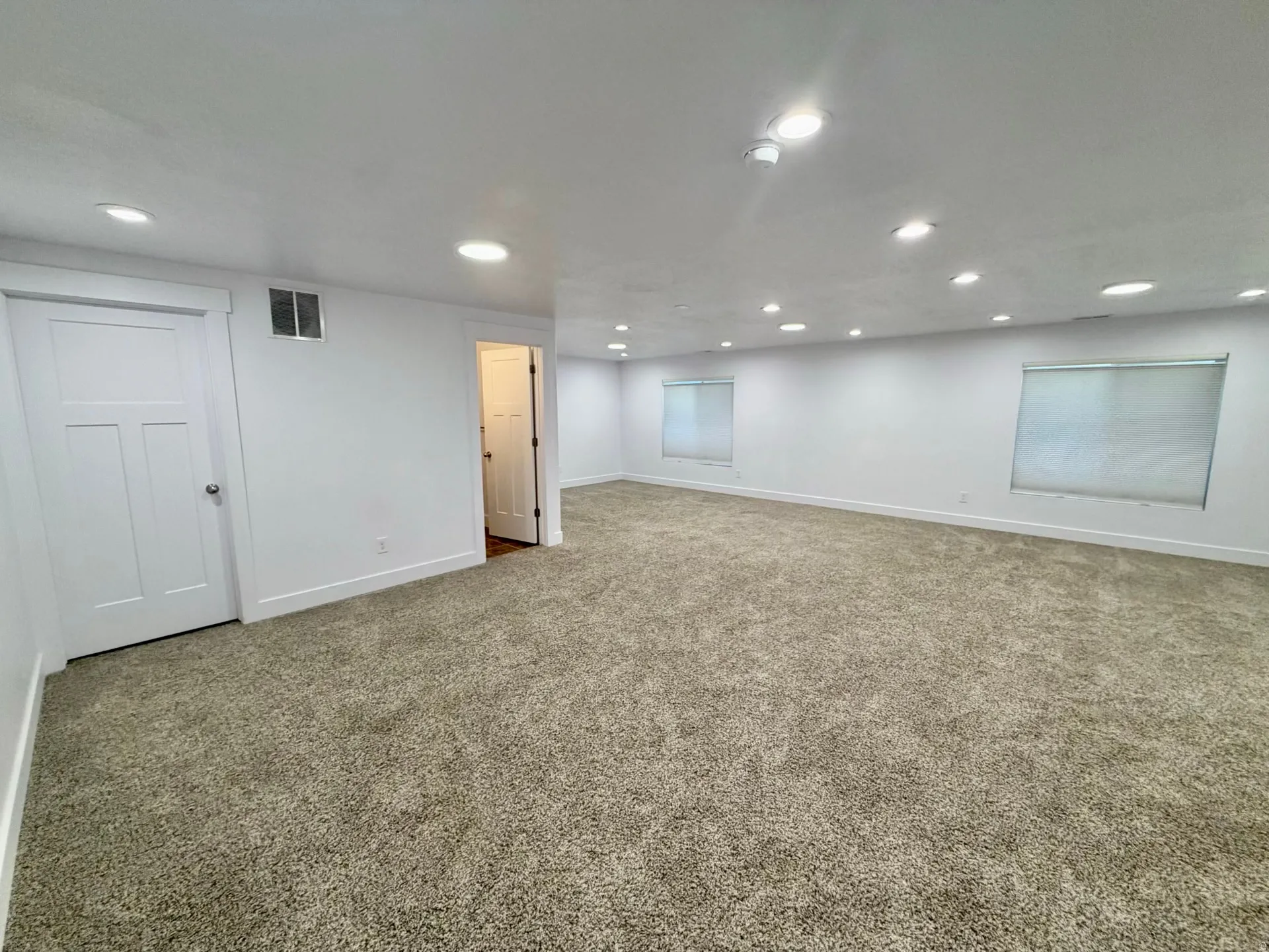 Spacious room featuring new carpeting, recessed ceiling lighting, two windows with roller shades, and two panel doors
