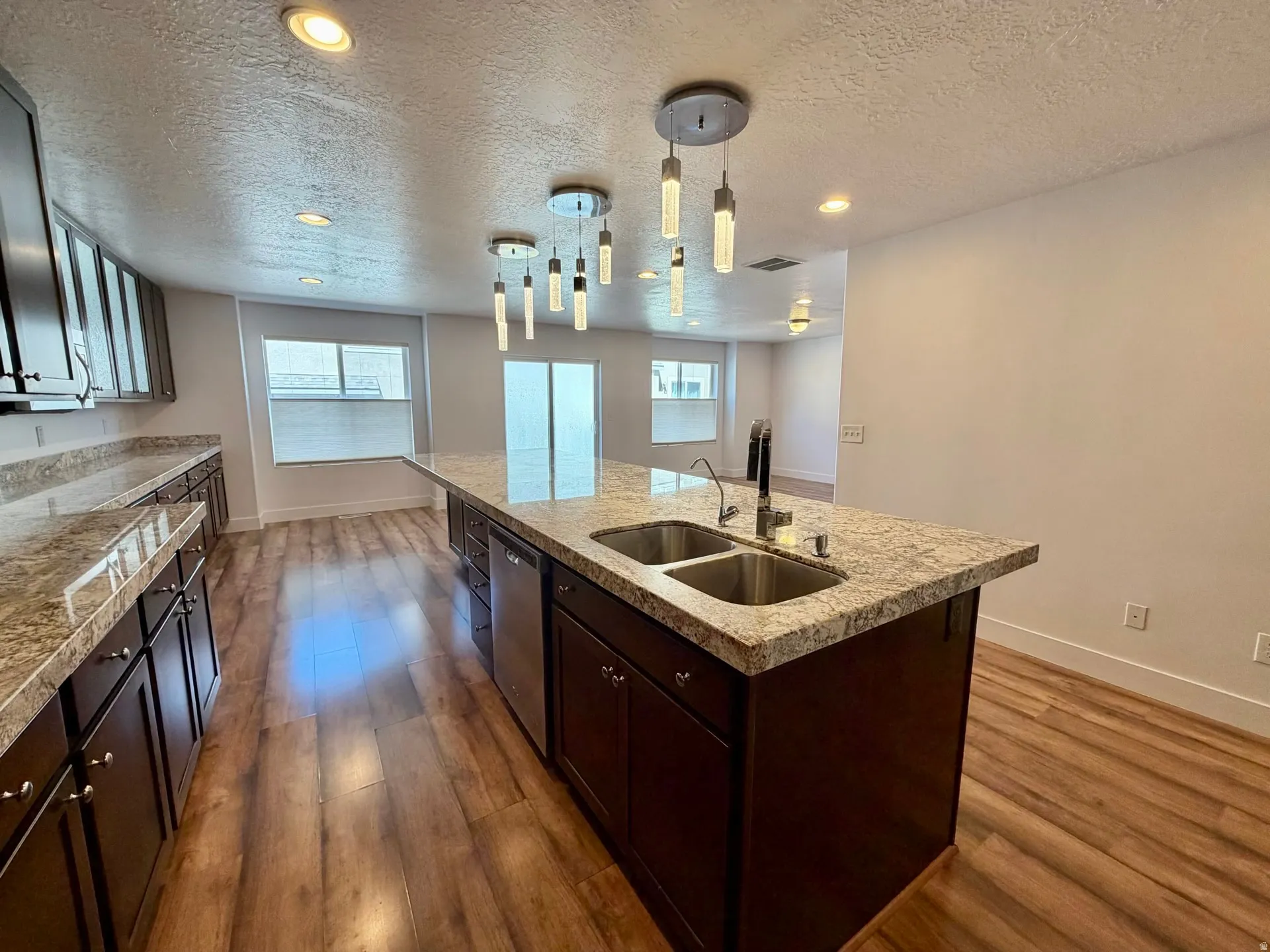 Expansive kitchen featuring a large island with a double basin sink, dark wood cabinetry, wood-finish flooring, recessed lighting, and a modern chandelier