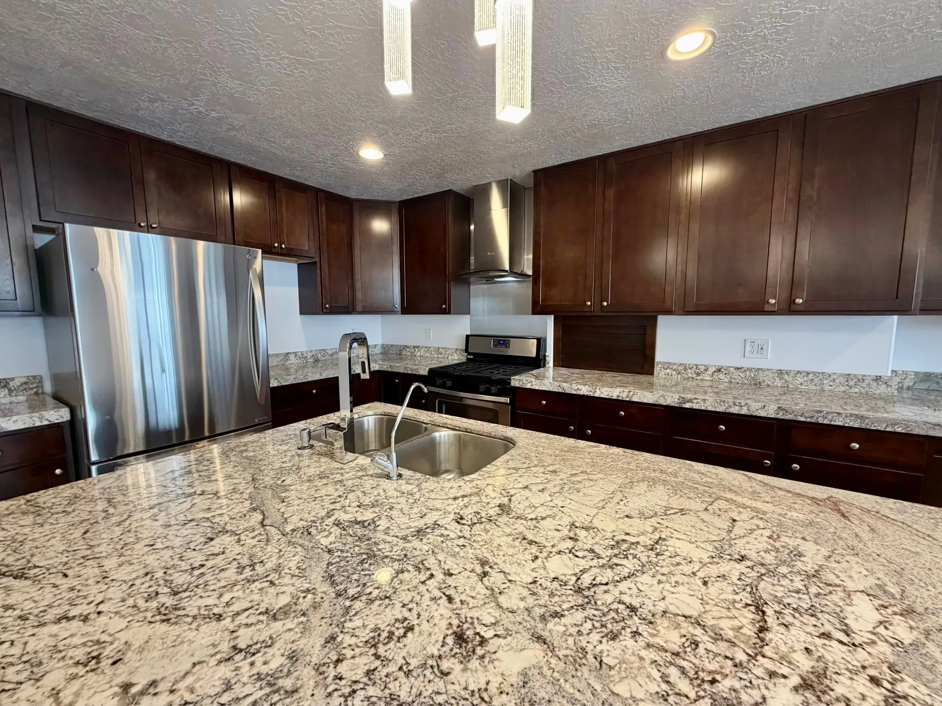 Spacious kitchen island featuring a double basin stainless steel sink, a pull-down faucet, and light-toned granite countertops