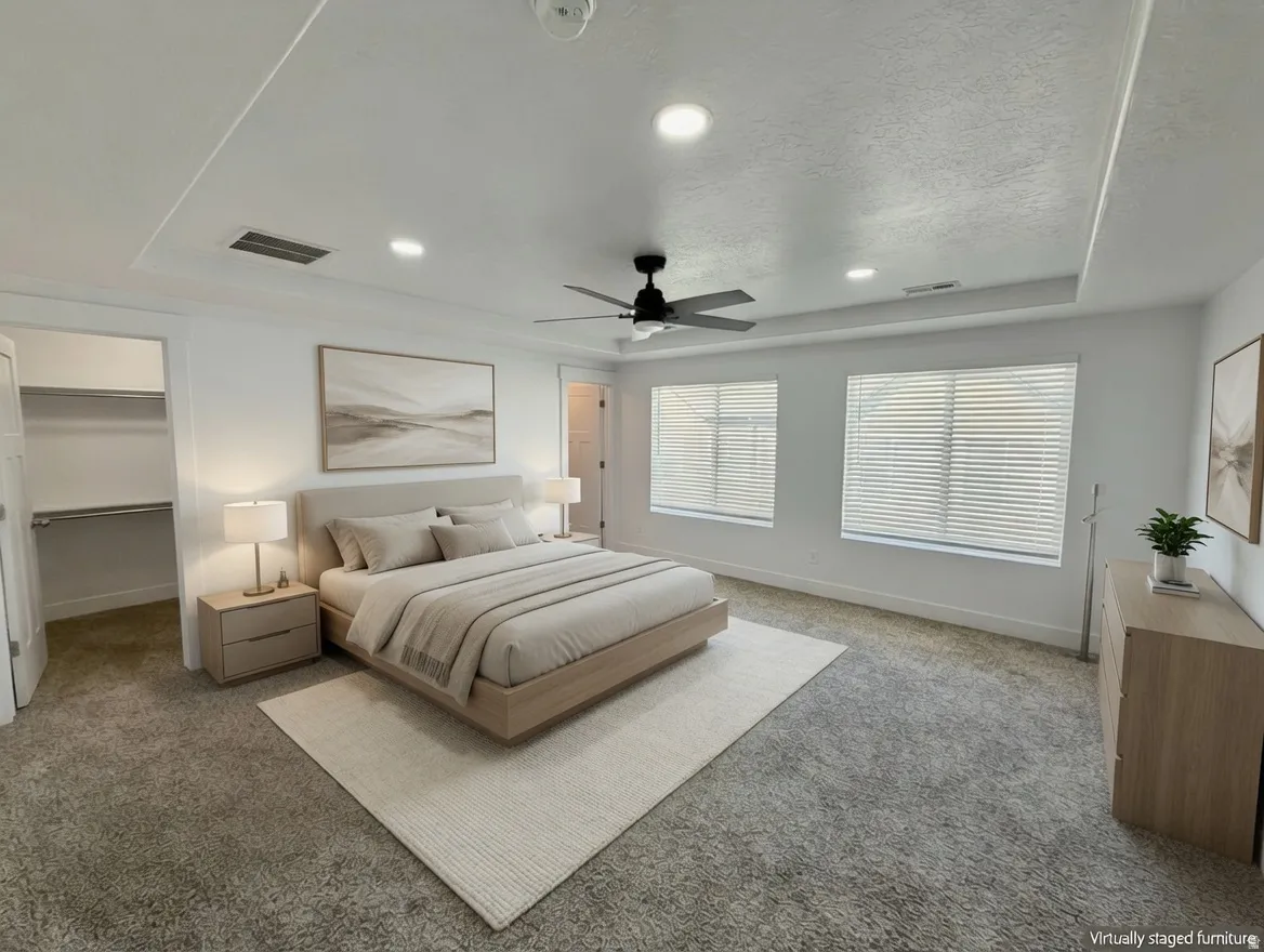 Spacious bedroom featuring a tray ceiling with recessed lighting, carpet flooring, and two large windows with blinds