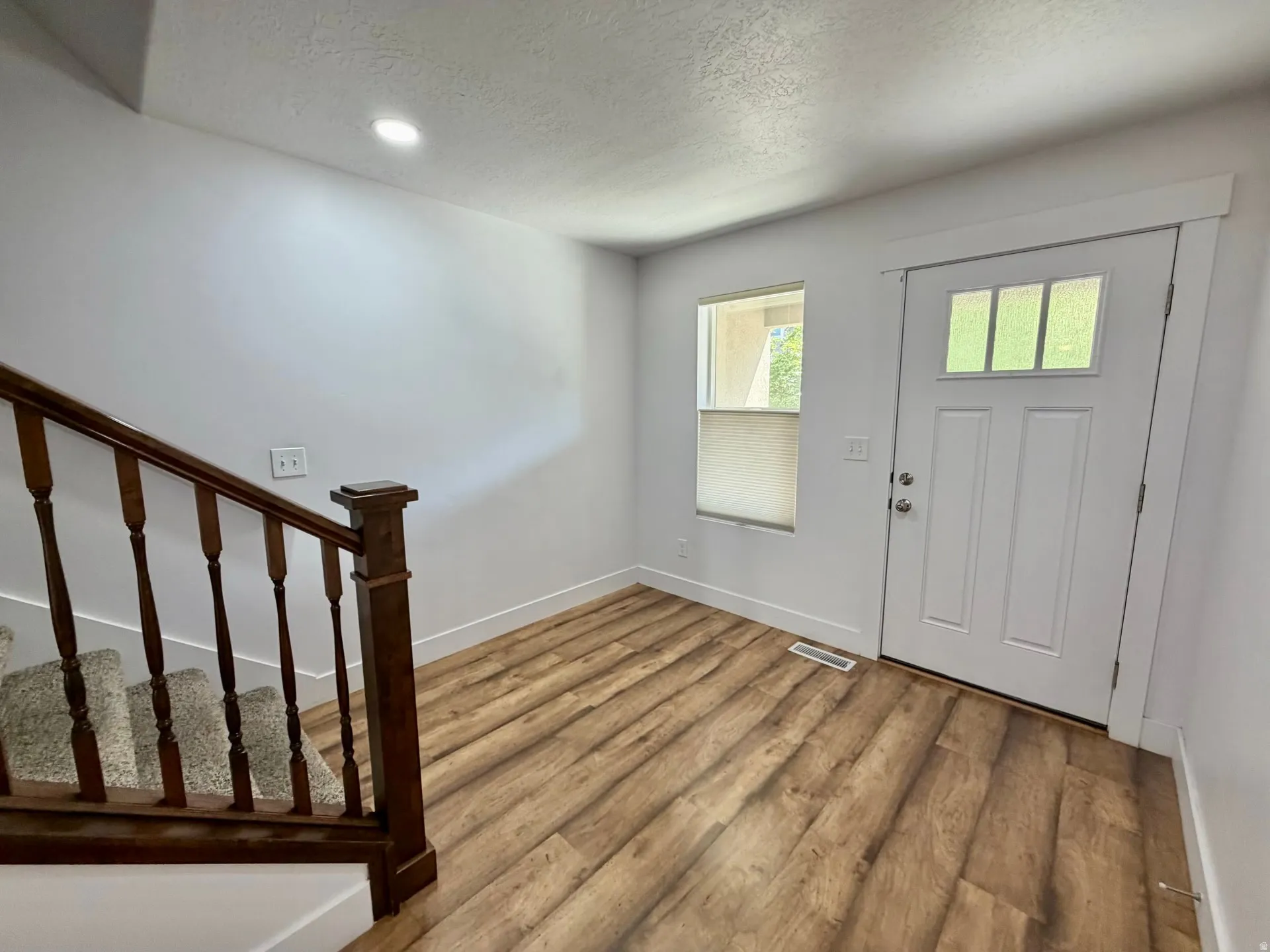 Entryway featuring wood-finish flooring, a contemporary white front door with upper glass panels, and a staircase with a wooden banister