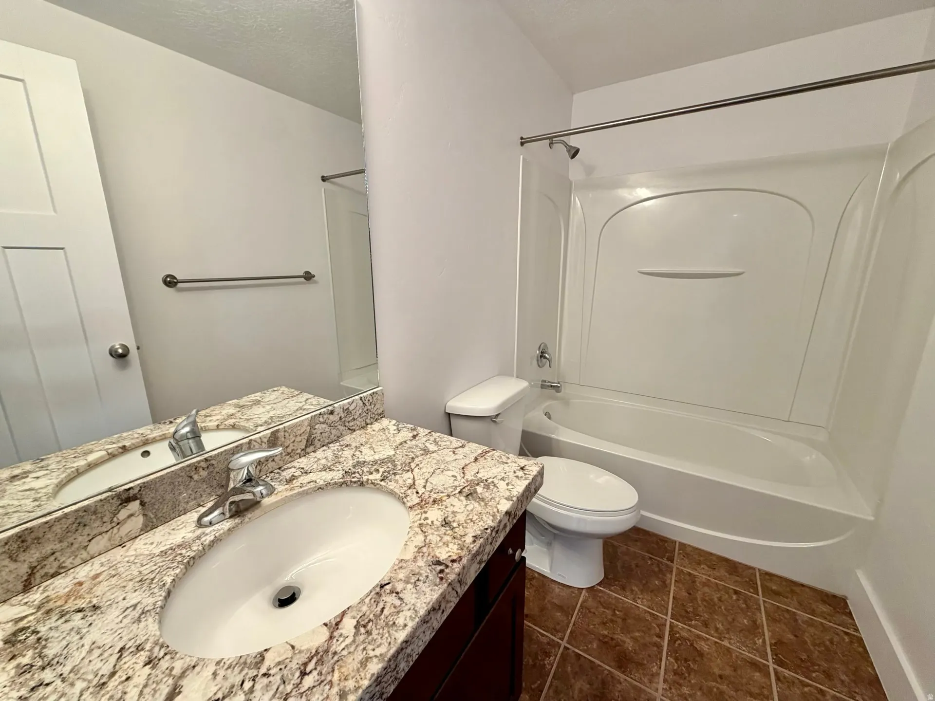 Bathroom featuring a granite-look vanity with an undermount sink, ceramic tile flooring, a white toilet, and a white bathtub with an integrated shower