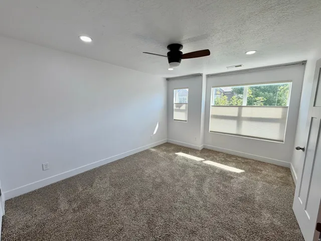 Carpeted interior space featuring recessed lighting, a ceiling fan with integrated light, and multiple windows with privacy shades