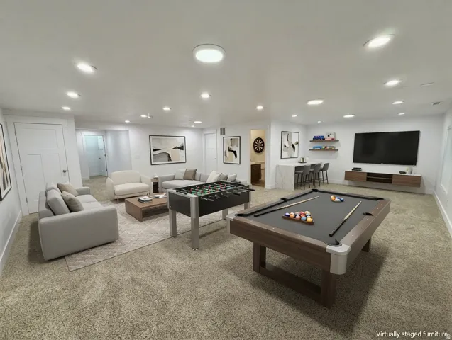 Spacious entertainment room featuring recessed lighting, a built-in bar with seating, floating wall shelving, and a wall-mounted media console