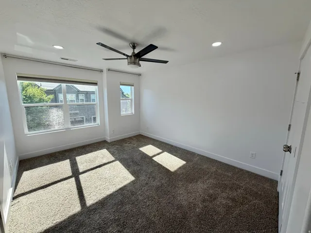 Carpeted room featuring a ceiling fan, recessed lighting, and two windows with blinds