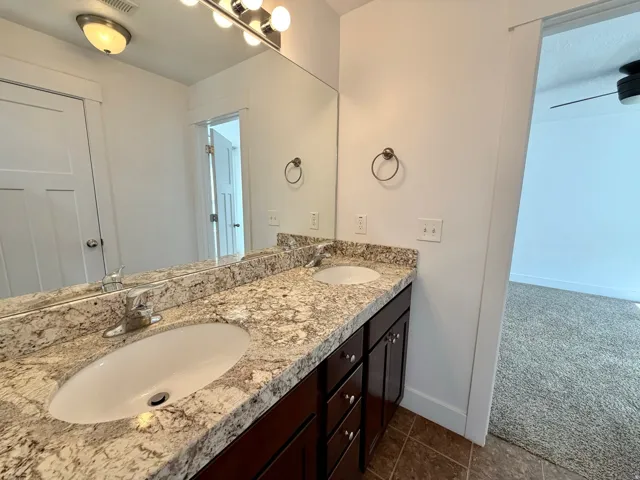 Double vanity featuring a light-toned stone countertop, dual undermount sinks, and dark wood-finish cabinetry