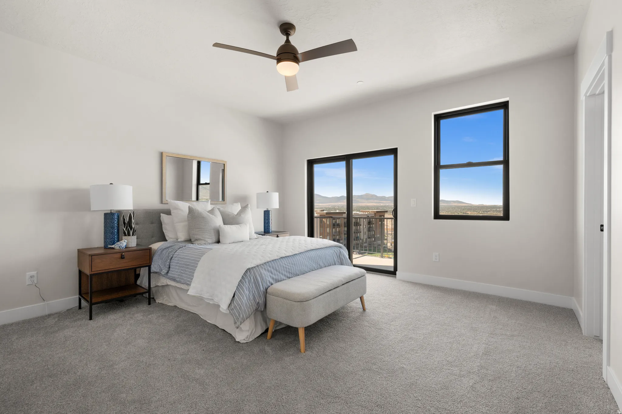 Spacious room featuring light gray carpeting, a ceiling fan with integrated lighting, and multiple windows with dark frames