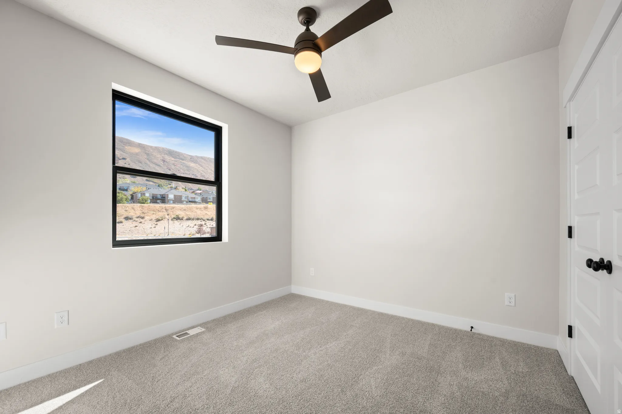 Carpeted room featuring a ceiling fan with integrated lighting, a window with a black frame, and a white paneled door with black hardware