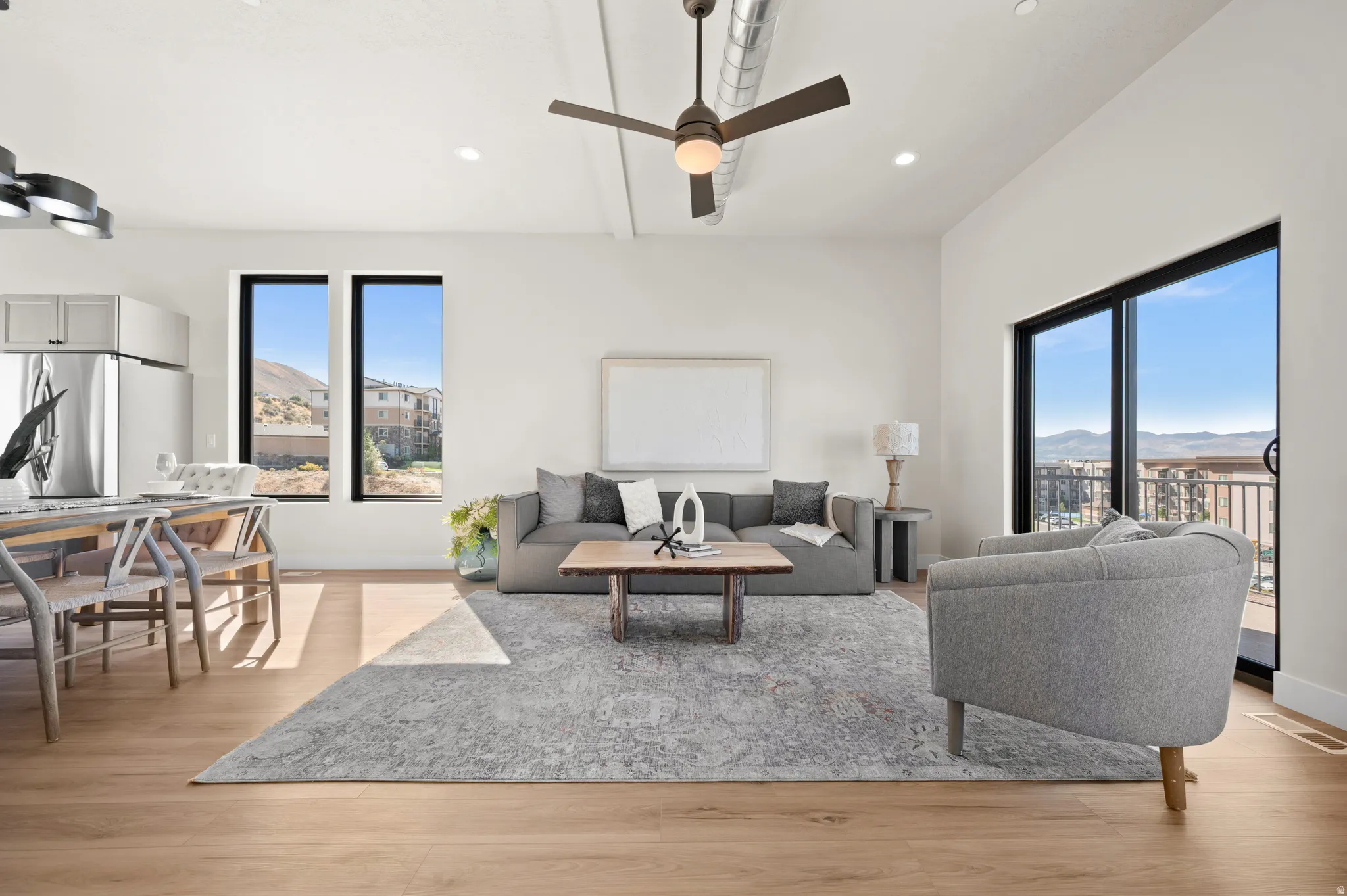 Expansive open-concept living area featuring light wood-finish flooring, a contemporary ceiling fan with integrated lighting, and high ceilings