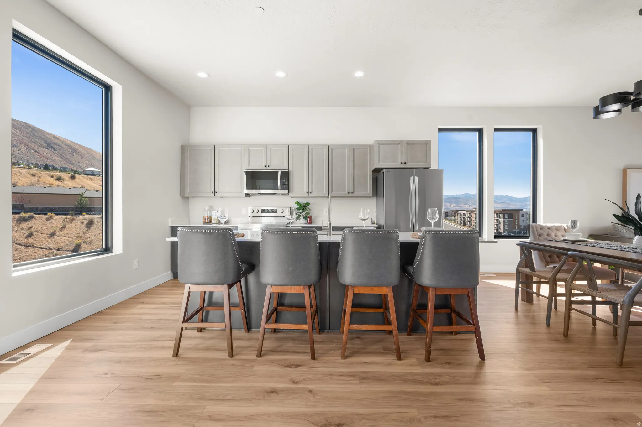 Open-concept living space with wood-finish flooring, a kitchen island, gray cabinetry, stainless steel appliances, and large windows