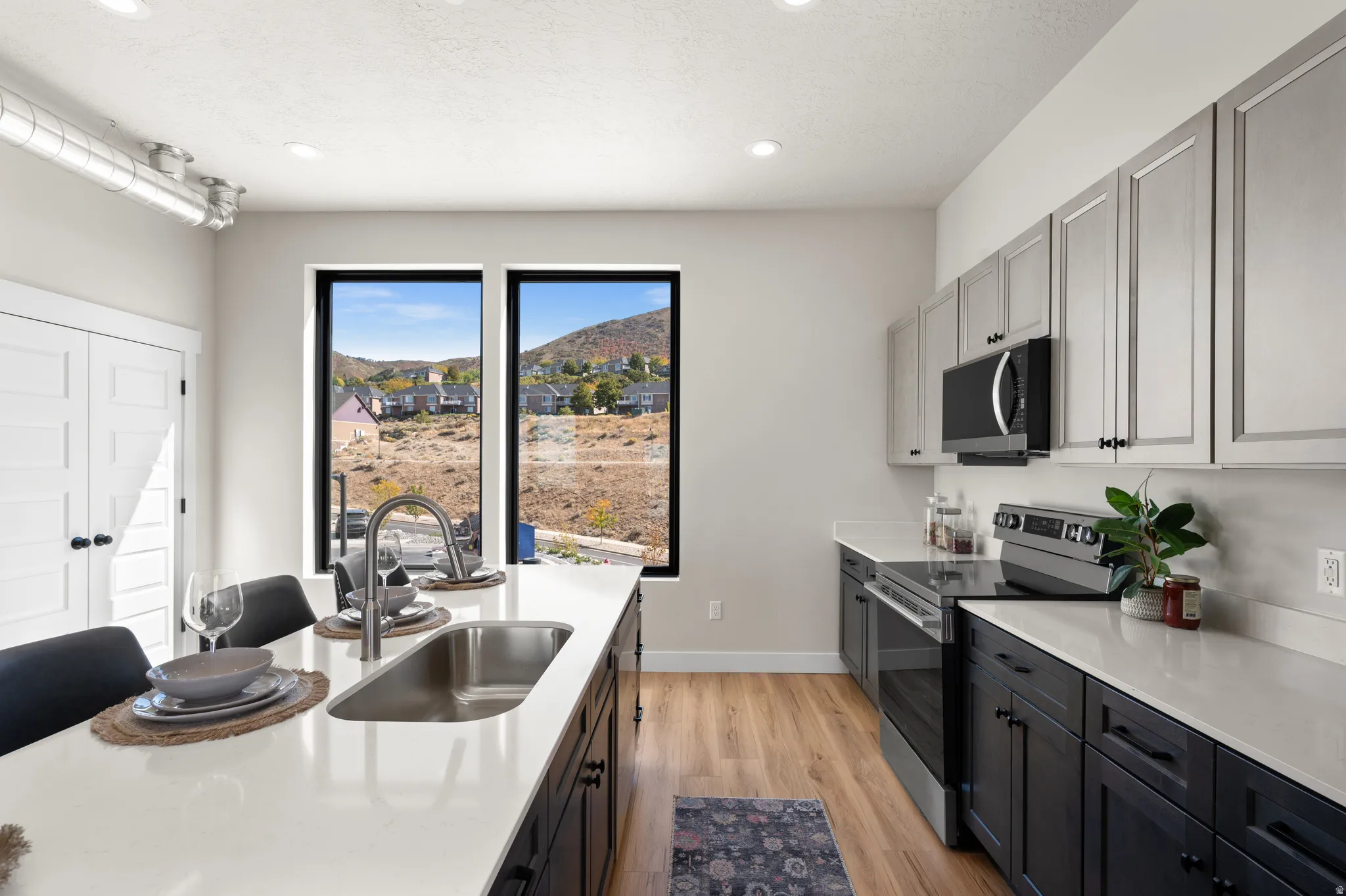 Contemporary kitchen featuring a large island with an undermount sink, light-toned countertops, two-tone cabinetry, stainless steel appliances, and wood-finish flooring