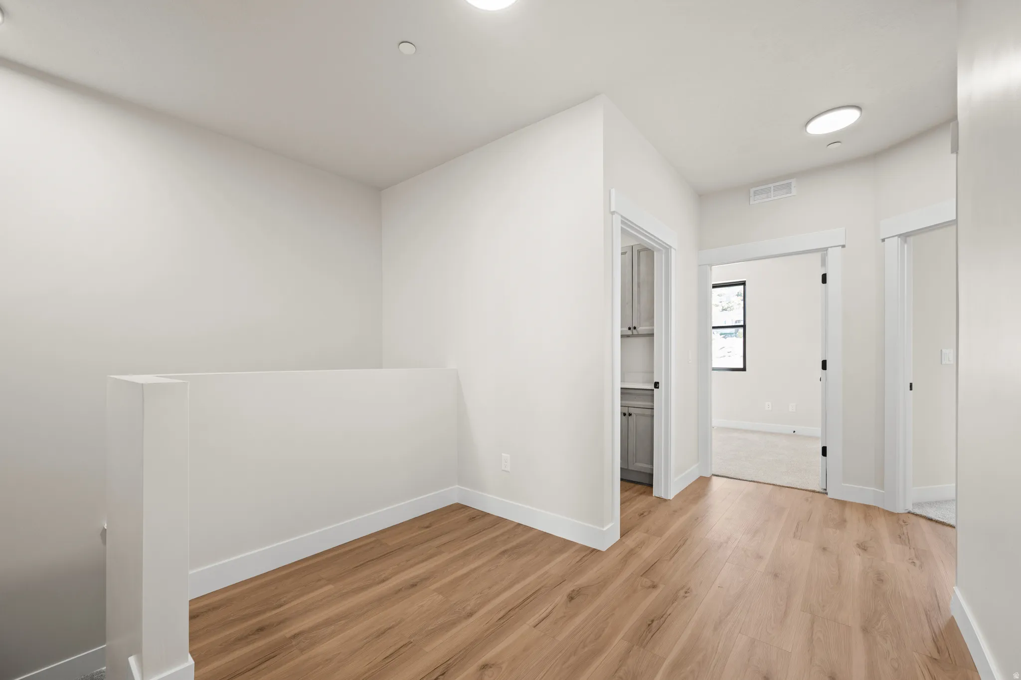 Hallway featuring wood-finish flooring, white trim, recessed lighting, and a pantry with gray cabinetry