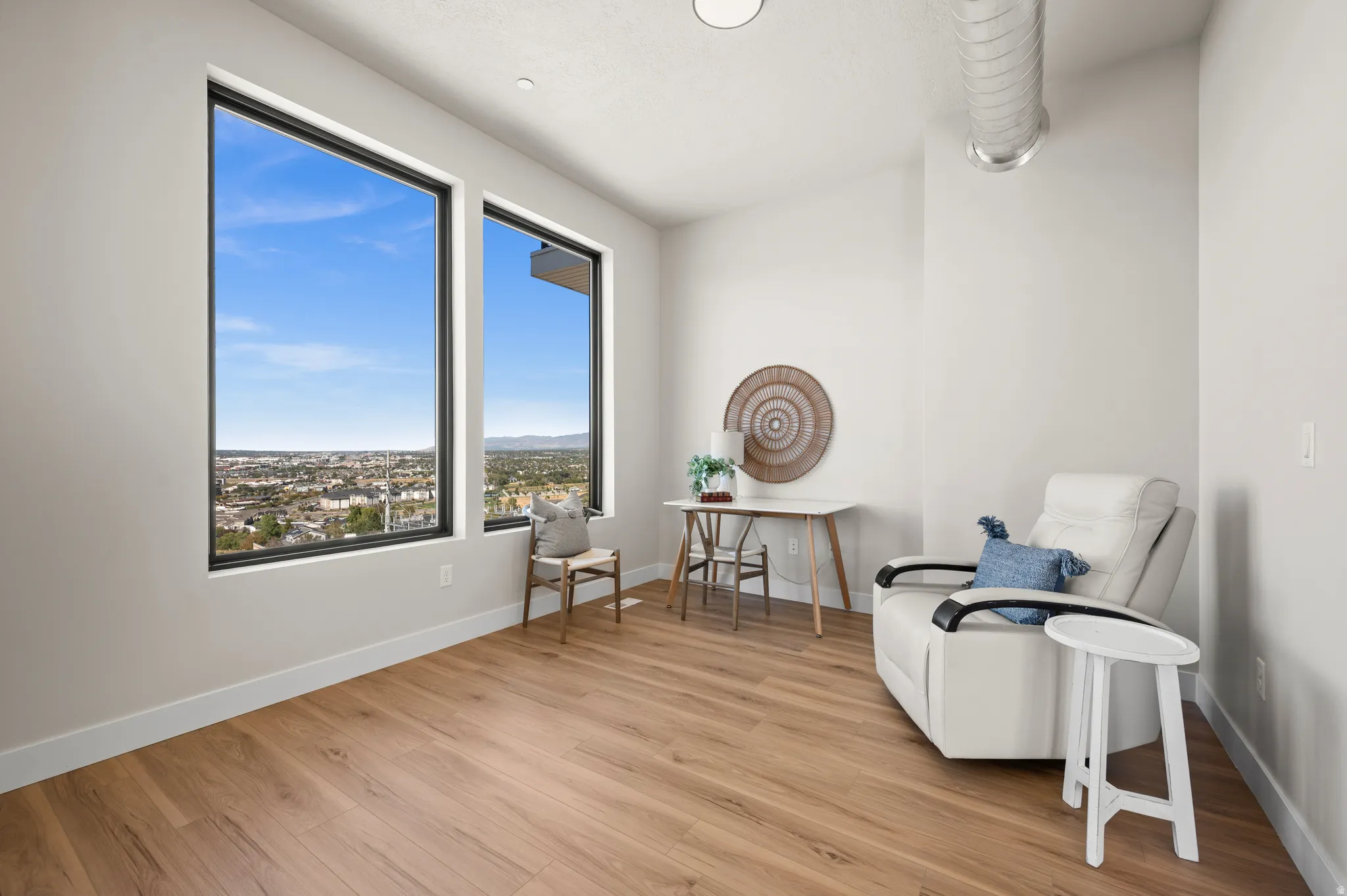 Room featuring expansive windows with black frames, wood-finish flooring, white baseboards, and a high ceiling with exposed ductwork