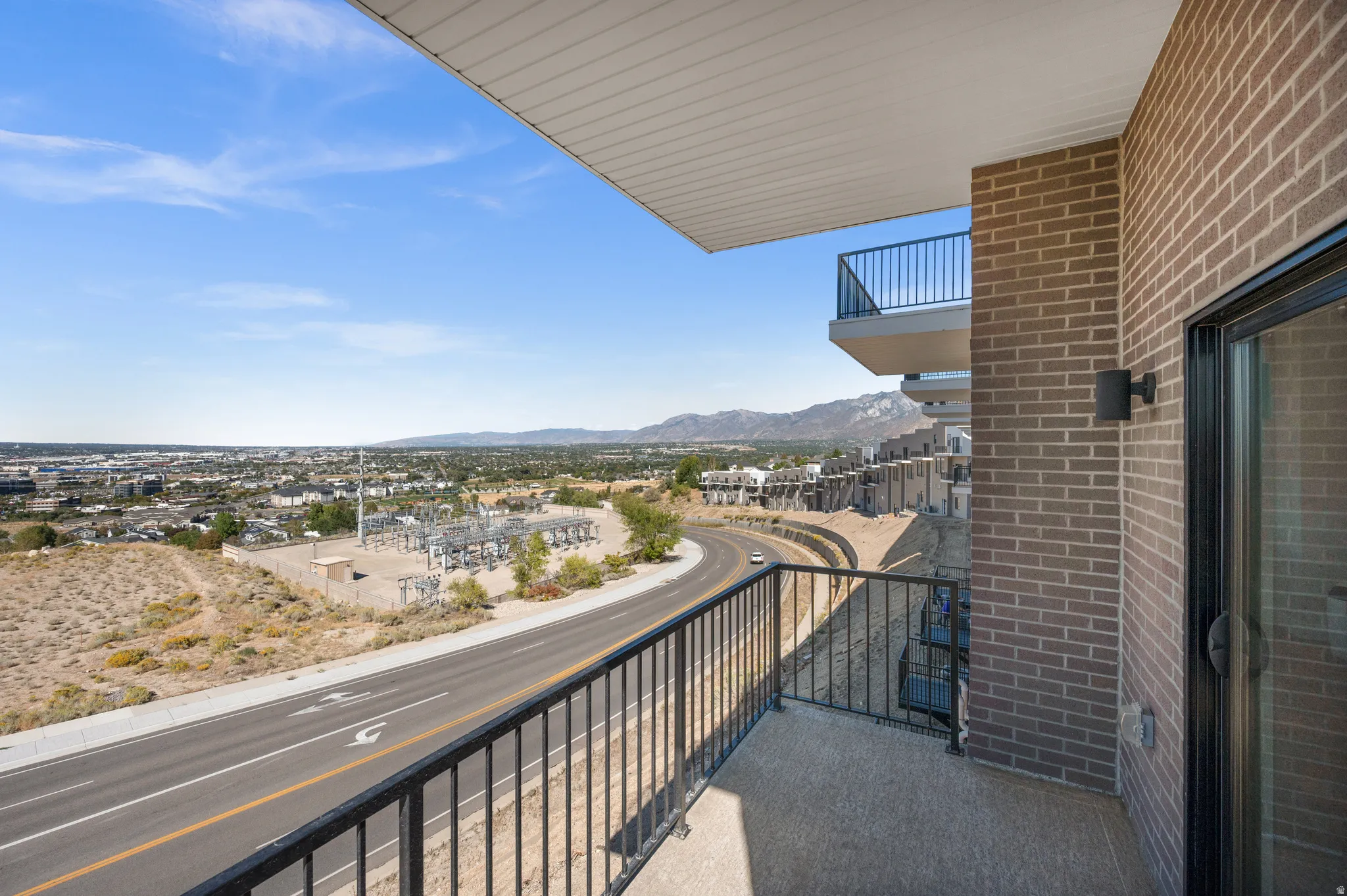 Private balcony featuring a textured concrete floor, black metal railing, and brick exterior wall