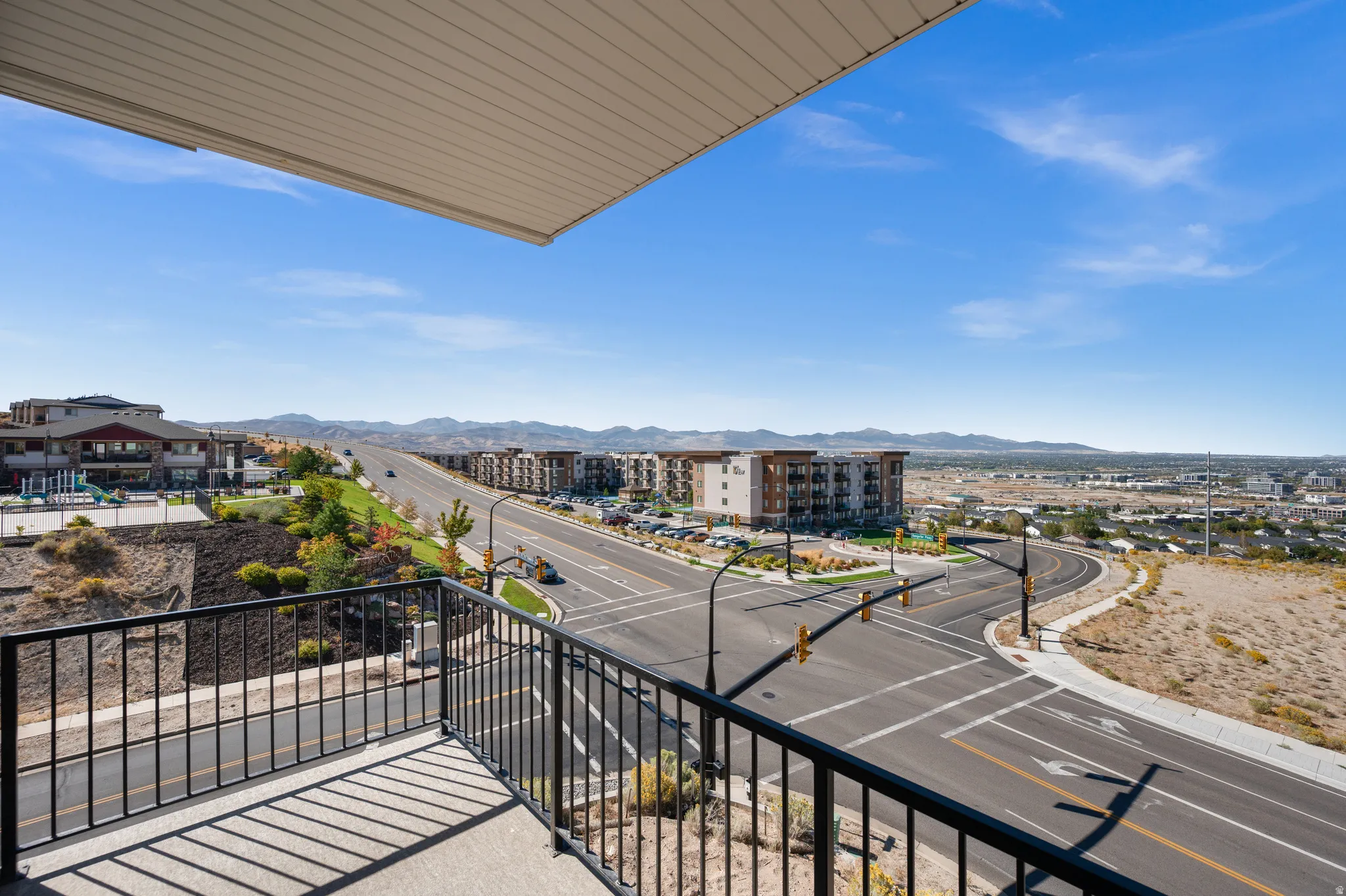 Balcony with black metal railing overlooking a paved intersection and distant mountains
