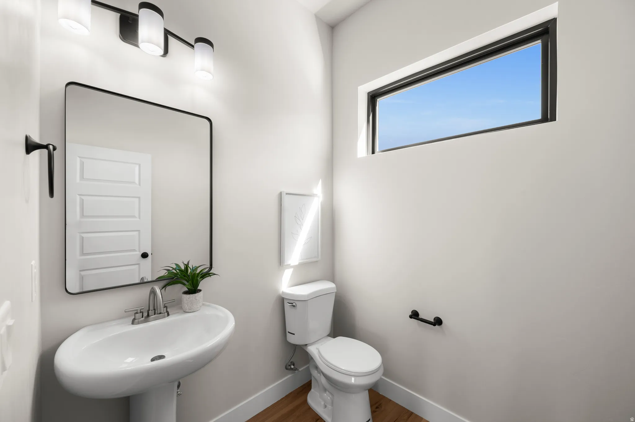 Contemporary powder room featuring a pedestal sink with a chrome faucet, a rectangular mirror with a black frame, and a horizontal window with a black frame