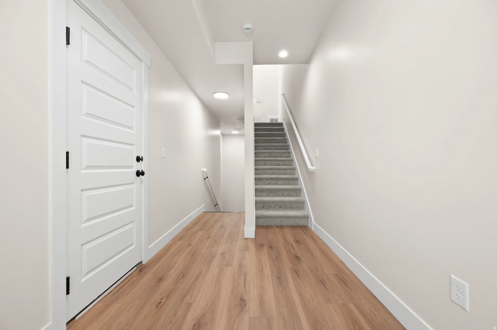 Entryway featuring light wood-finish flooring, a contemporary five-panel door with matte black hardware, and crisp white baseboards