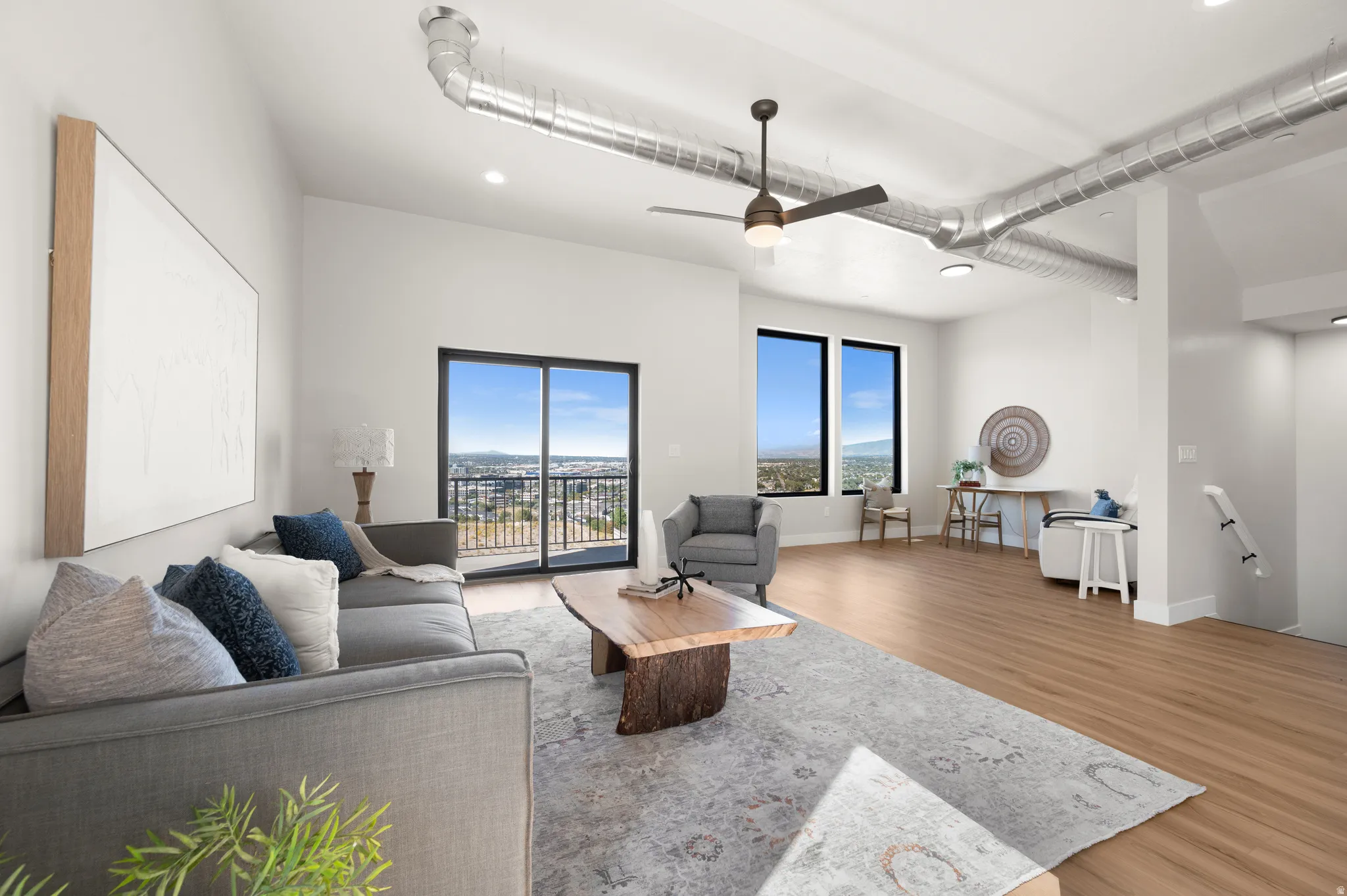 Spacious living area featuring exposed ductwork, a ceiling fan, and light wood-finish flooring