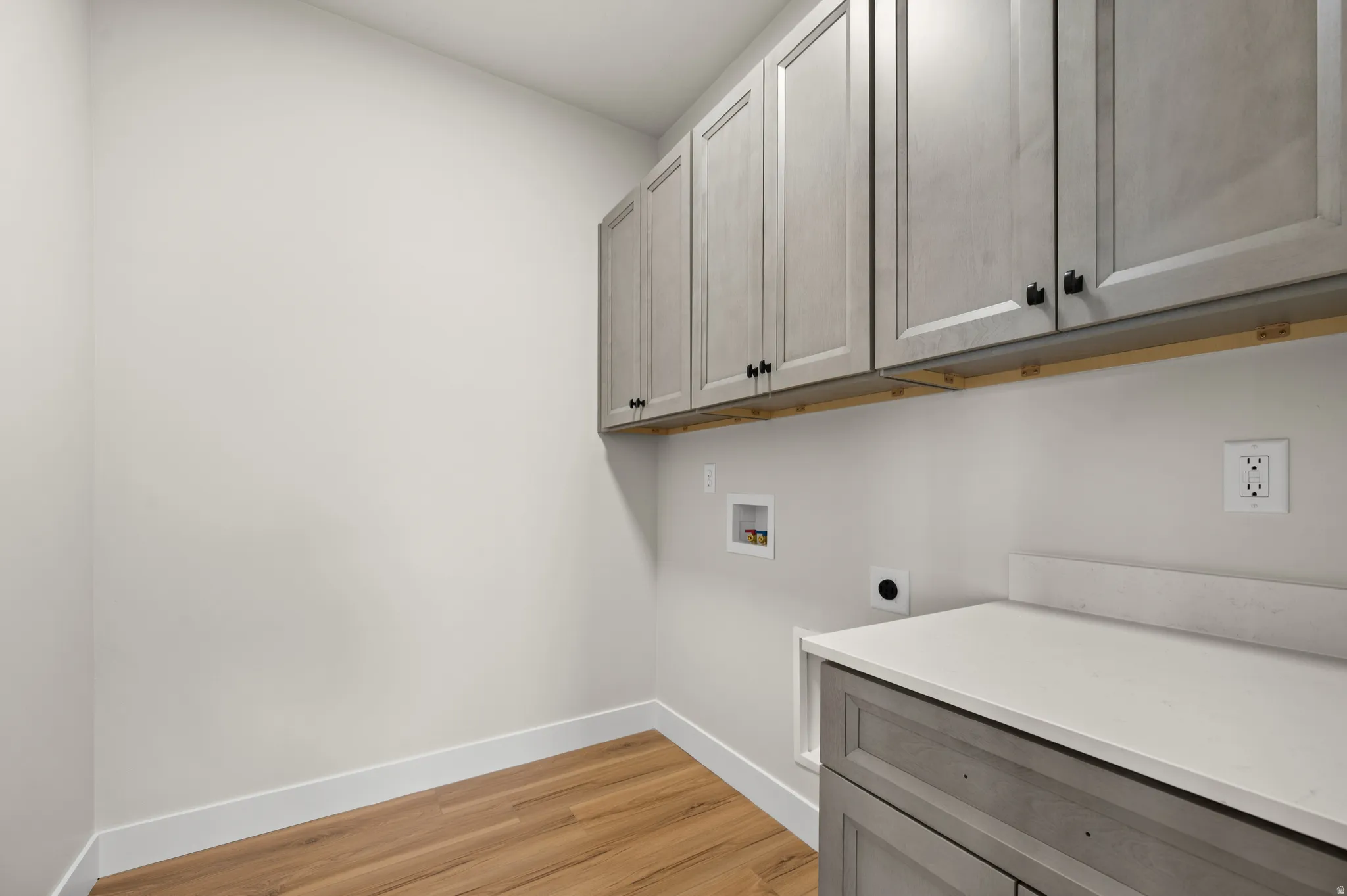 Laundry area featuring wood-finish flooring, extensive upper cabinetry, base cabinetry with a light-toned countertop, and white baseboards