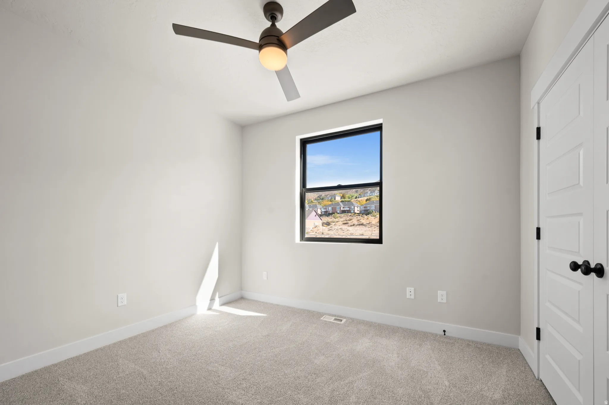 Spacious room featuring neutral carpeting, a contemporary ceiling fan with integrated lighting, and a window with a black frame