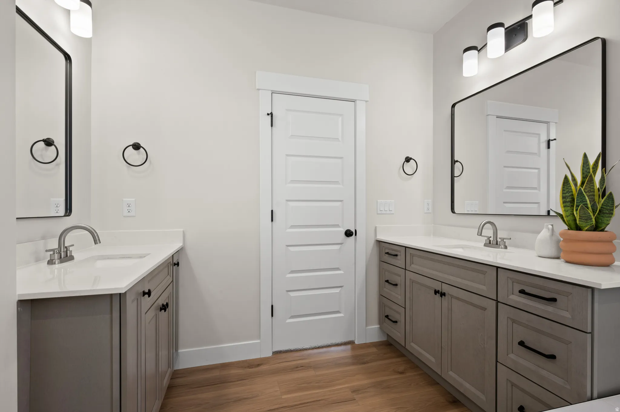 Bathroom featuring dual vanities with gray cabinetry and white countertops, wood-finish flooring, and black framed mirrors