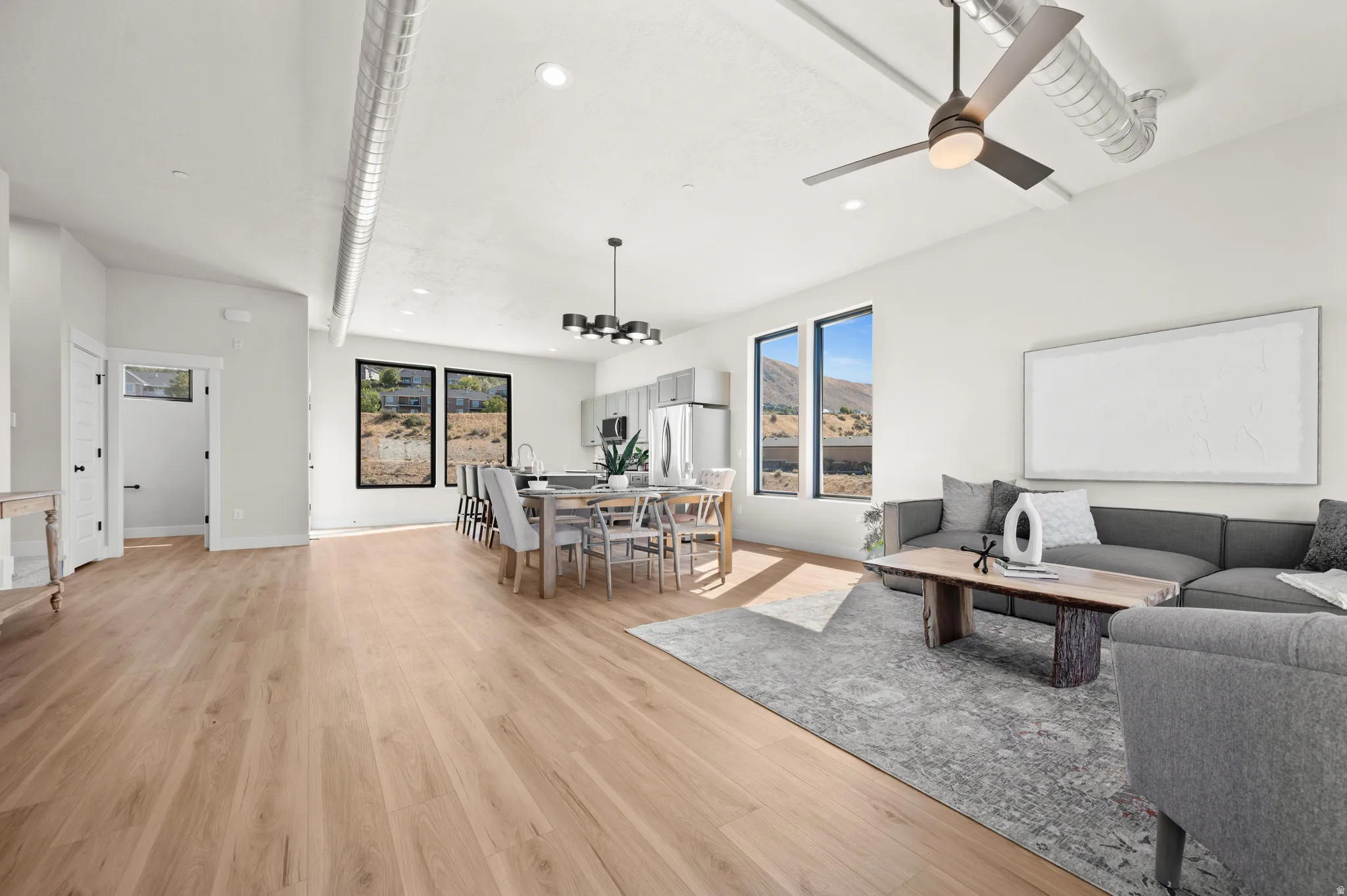 Open-concept living area featuring light wood-finish flooring, high ceilings with exposed ductwork, and recessed lighting
