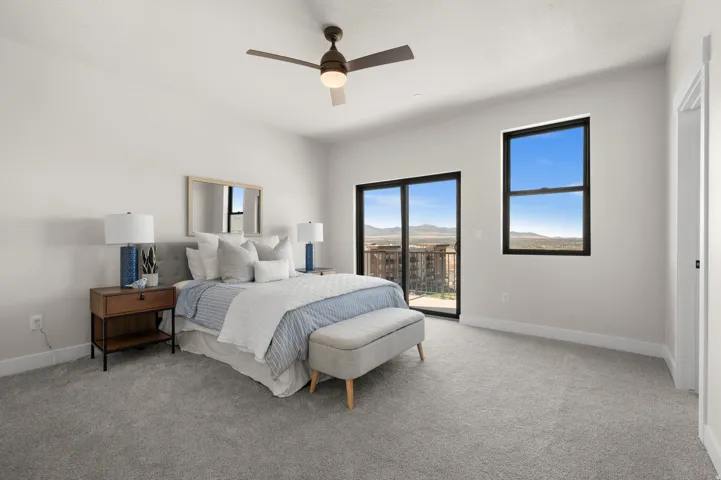 Spacious room featuring light gray carpeting, a ceiling fan with integrated lighting, and multiple windows with dark frames