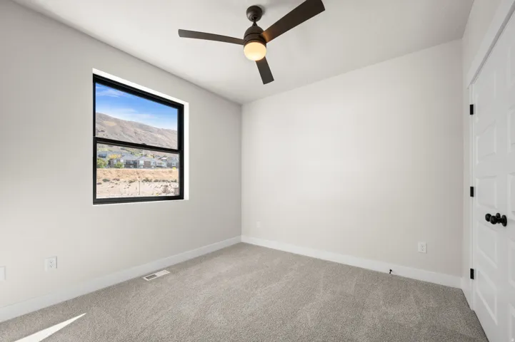 Carpeted room featuring a ceiling fan with integrated lighting, a window with a black frame, and a white paneled door with black hardware