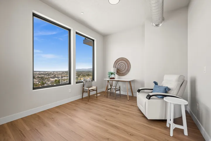 Room featuring expansive windows with black frames, wood-finish flooring, white baseboards, and a high ceiling with exposed ductwork