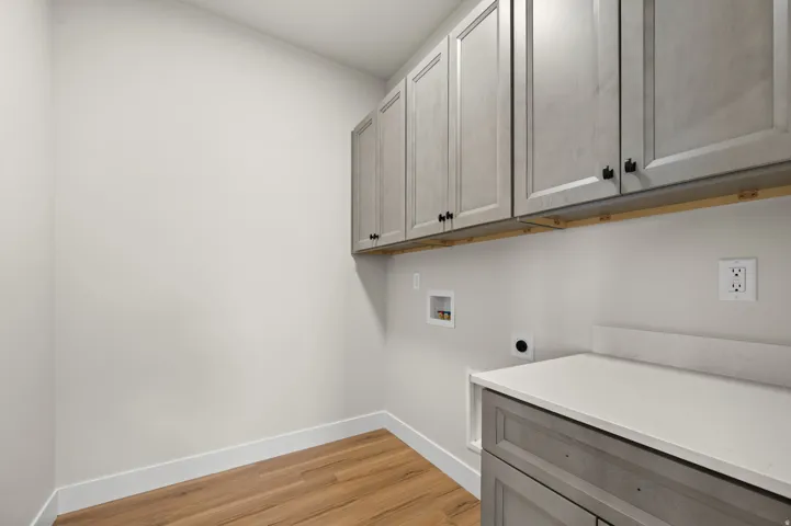 Laundry area featuring wood-finish flooring, extensive upper cabinetry, base cabinetry with a light-toned countertop, and white baseboards