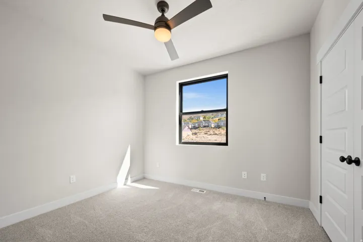 Spacious room featuring neutral carpeting, a contemporary ceiling fan with integrated lighting, and a window with a black frame