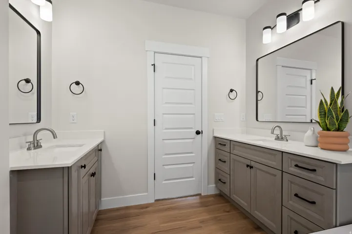 Bathroom featuring dual vanities with gray cabinetry and white countertops, wood-finish flooring, and black framed mirrors