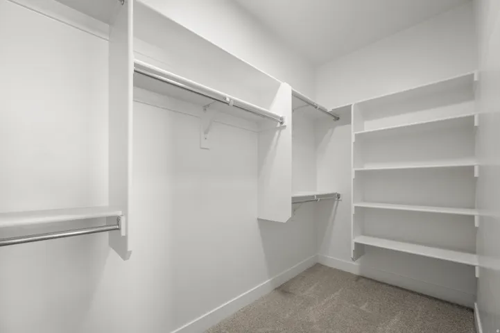 Walk-in closet featuring built-in shelving, multiple hanging rods, and neutral-toned carpet flooring