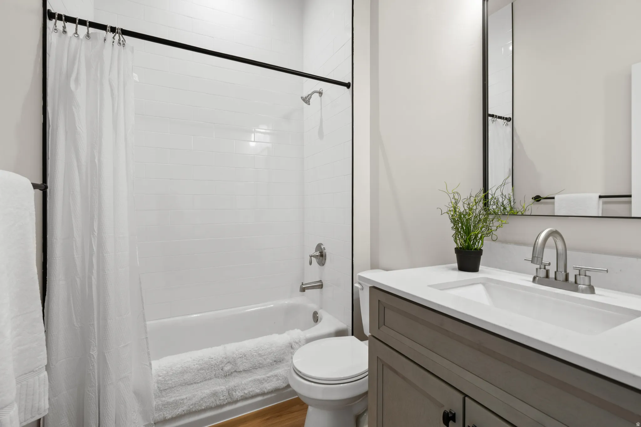 Full bathroom featuring a white subway tile shower surround, a white bathtub, and a wood-finish floor