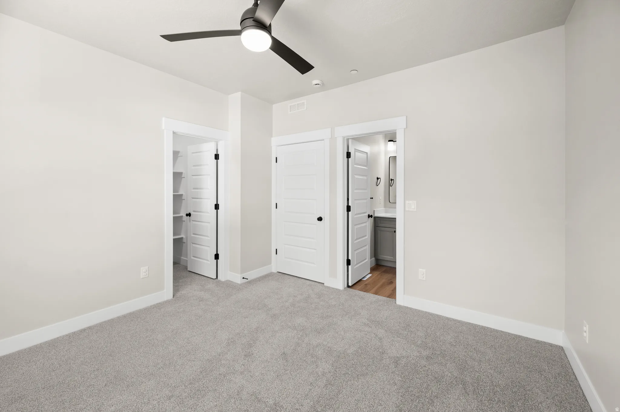 Carpeted room featuring a ceiling fan with integrated lighting, white trim work, and two paneled doors with black hardware