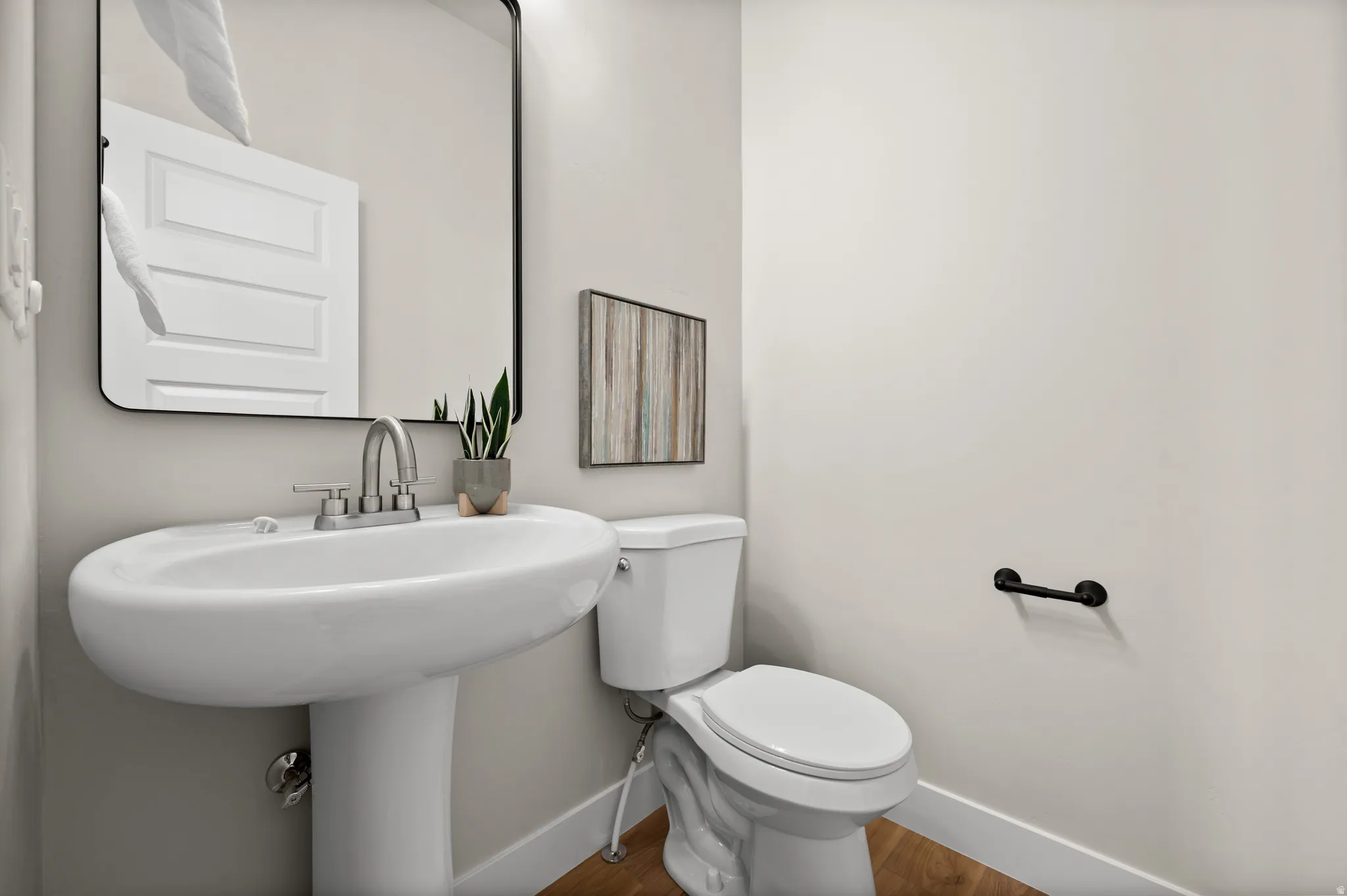 Pedestal sink with chrome faucet, complemented by a rectangular mirror with a black frame