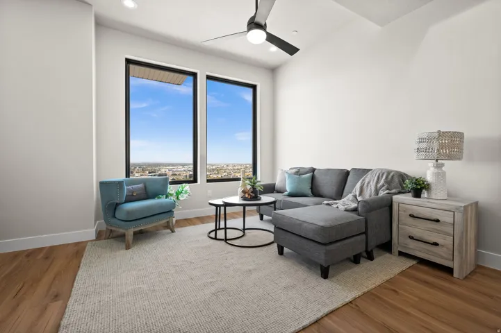 Two expansive windows frame the city skyline, complemented by a vaulted ceiling and a modern ceiling fan with integrated lighting