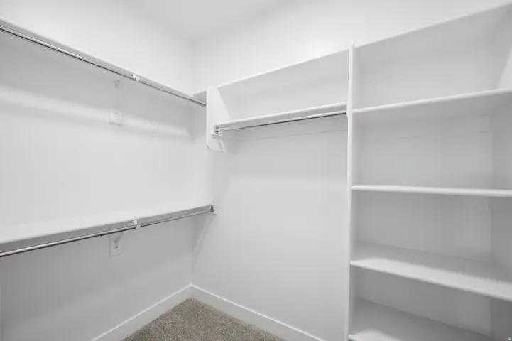 Walk-in closet featuring white shelving units, multiple hanging rods, and light-colored carpet flooring