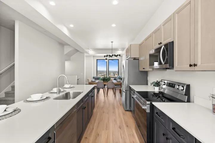 Modern kitchen featuring light wood-finish flooring, two-tone cabinetry, stainless steel appliances, white countertops, and a dual basin sink with a gooseneck faucet