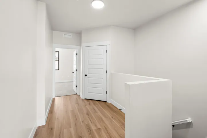 Upper-level landing featuring wood-finish flooring, white walls, five-panel interior doors with black hardware, and a partial staircase railing
